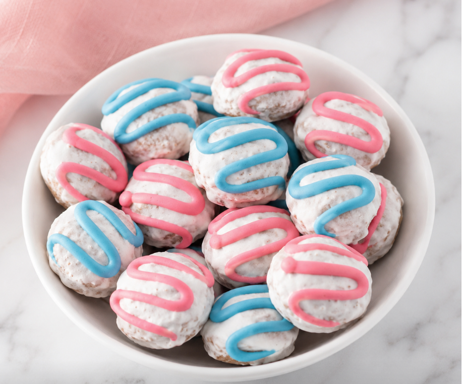 Organic Bon Bon Dog Treats decorated with pink and blue yogurt drizzle, arranged in a white bowl on a marble surface. Handmade peanut butter dog treats crafted in small batches with organic ingredients, creating a colorful bakery-style treat for dogs. 🐾💙🩷