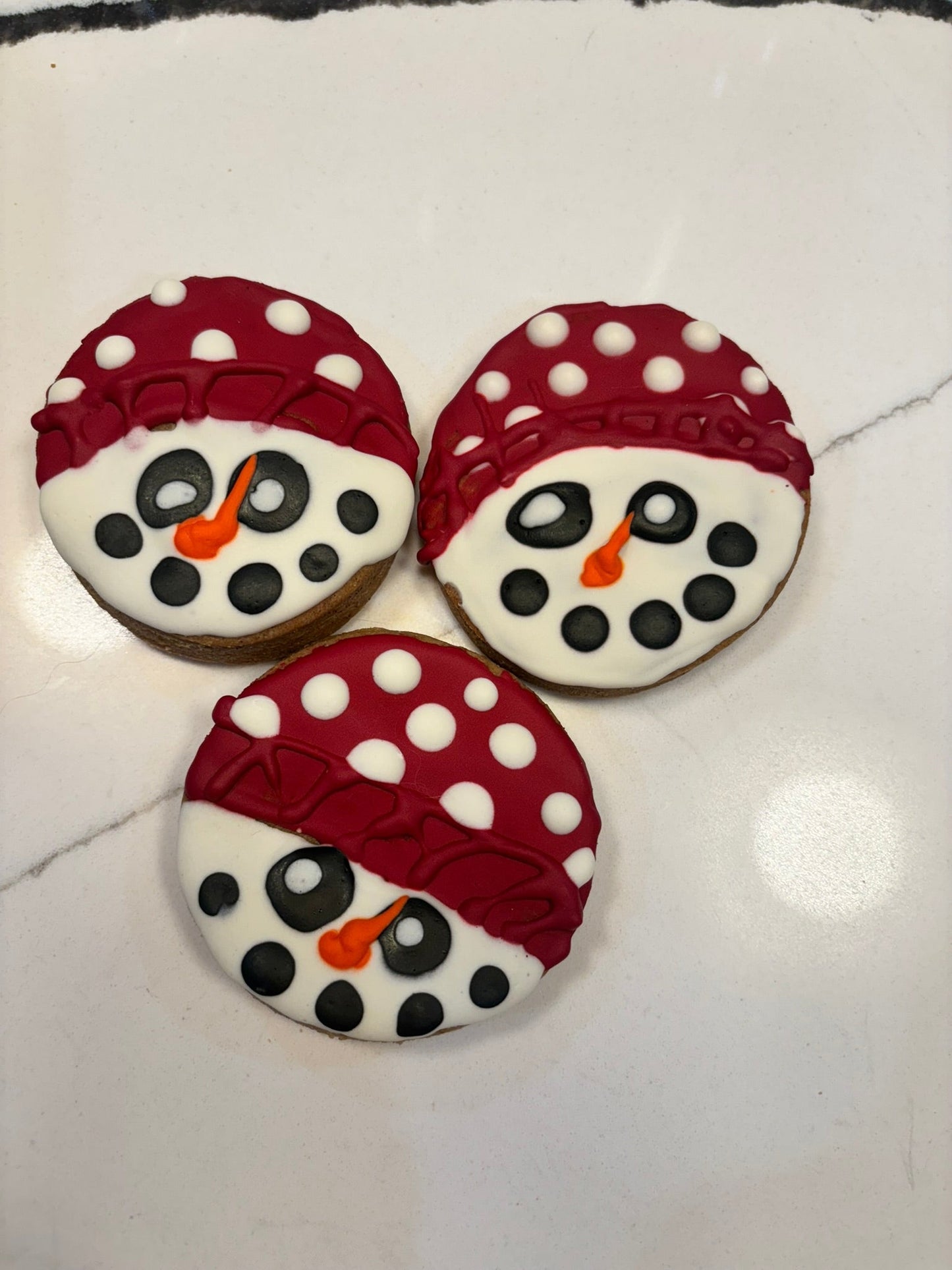 Three cookies decorated to look like snowmen on a white surface