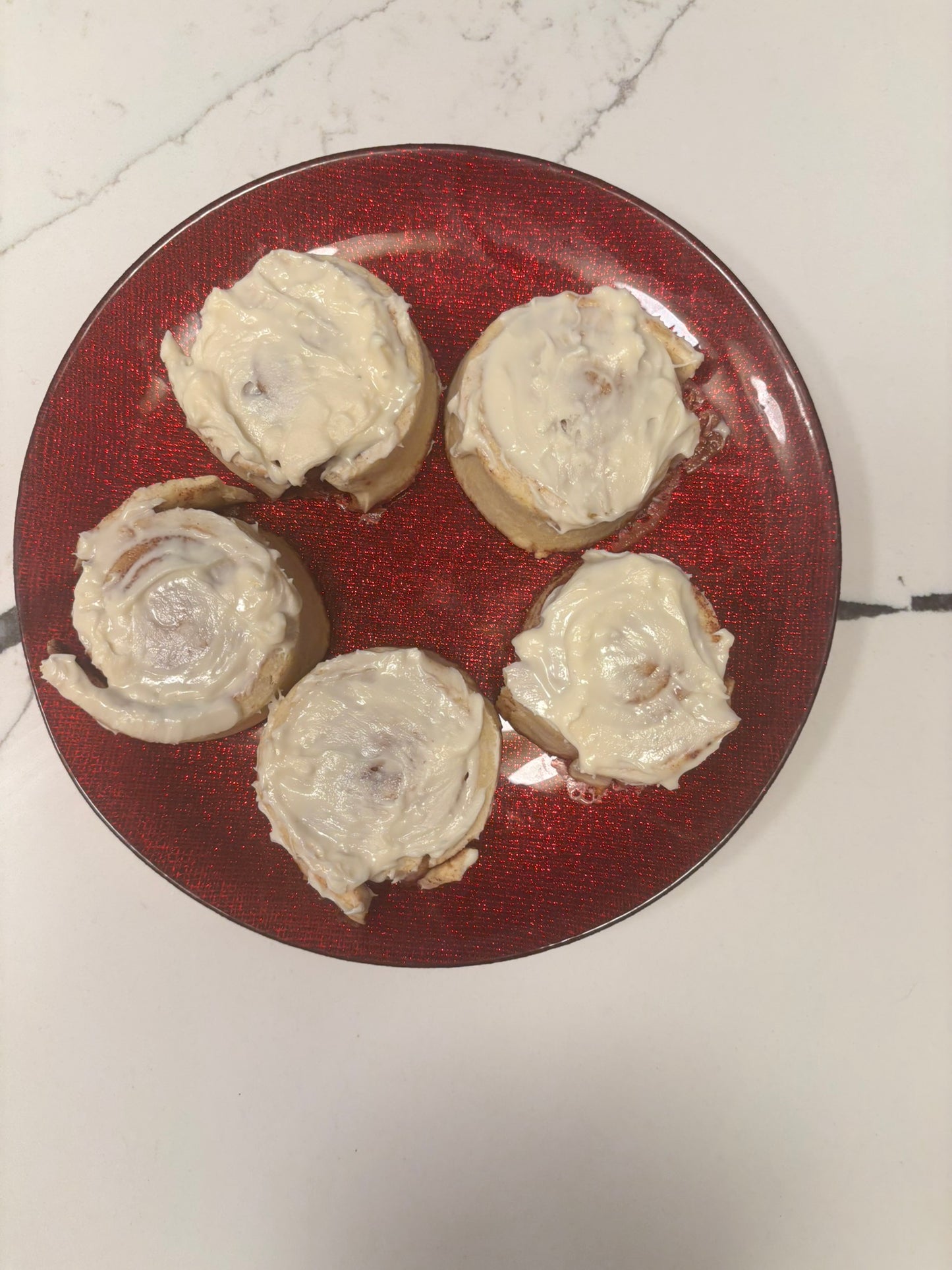 A plate of cinnamon bun-shaped organic dog treats with icing on top, placed on a decorative orange and yellow plate with ornate patterns.