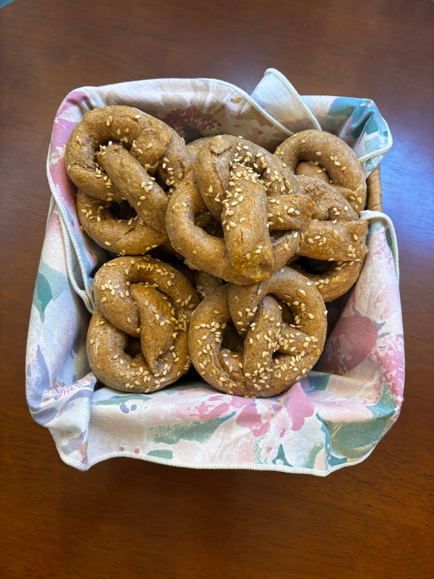 Handmade organic dog pretzel treats with sesame seeds in a basket lined with cloth on a wooden table