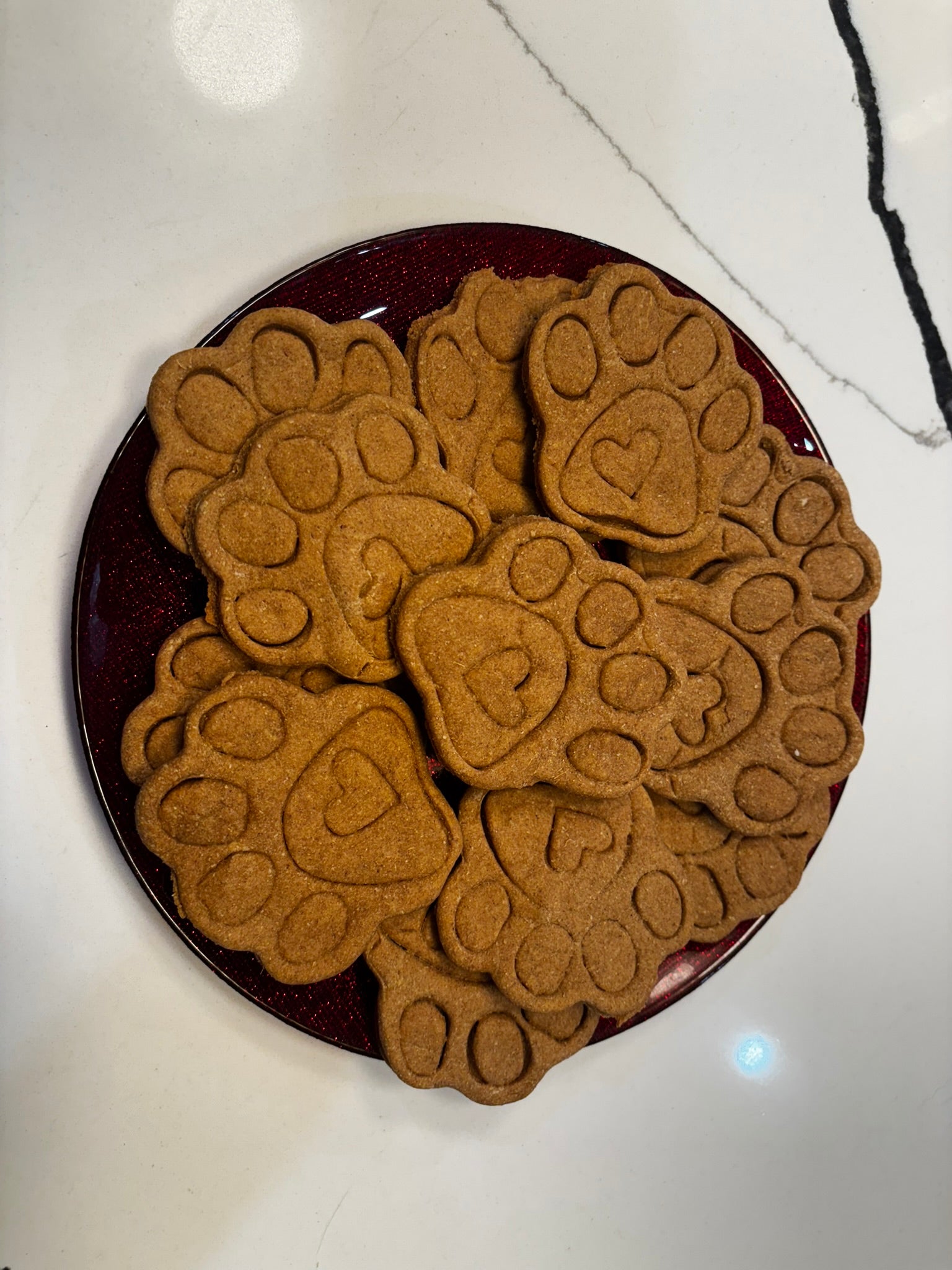 Top view of organic paw print dog cookies arranged on red plate, handmade dog bakery treats